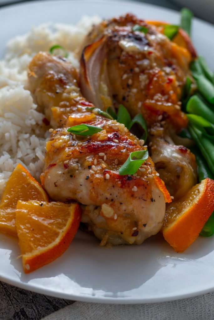 Closeup of sticky orange chicken drumsticks on a plate with rice and green beans.