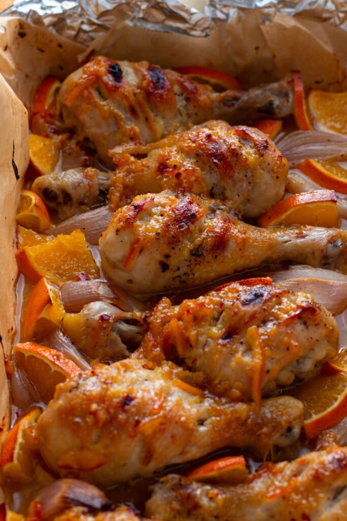Close up of baked sticky orange chicken drumsticks in a baking dish.