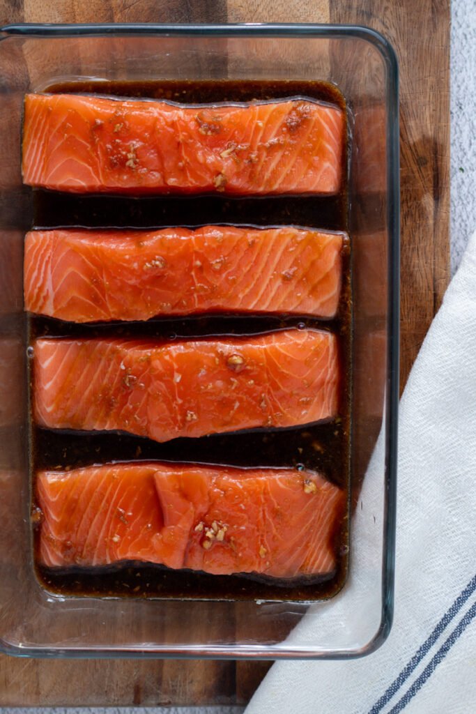 Unbaked salmon fillets in a baking dish with teriyaki sauce.