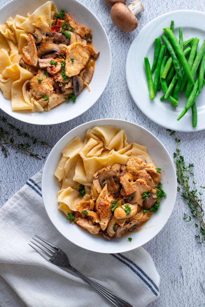 Two bowls of turkey stroganoff and a bowl of green beans seen from above.