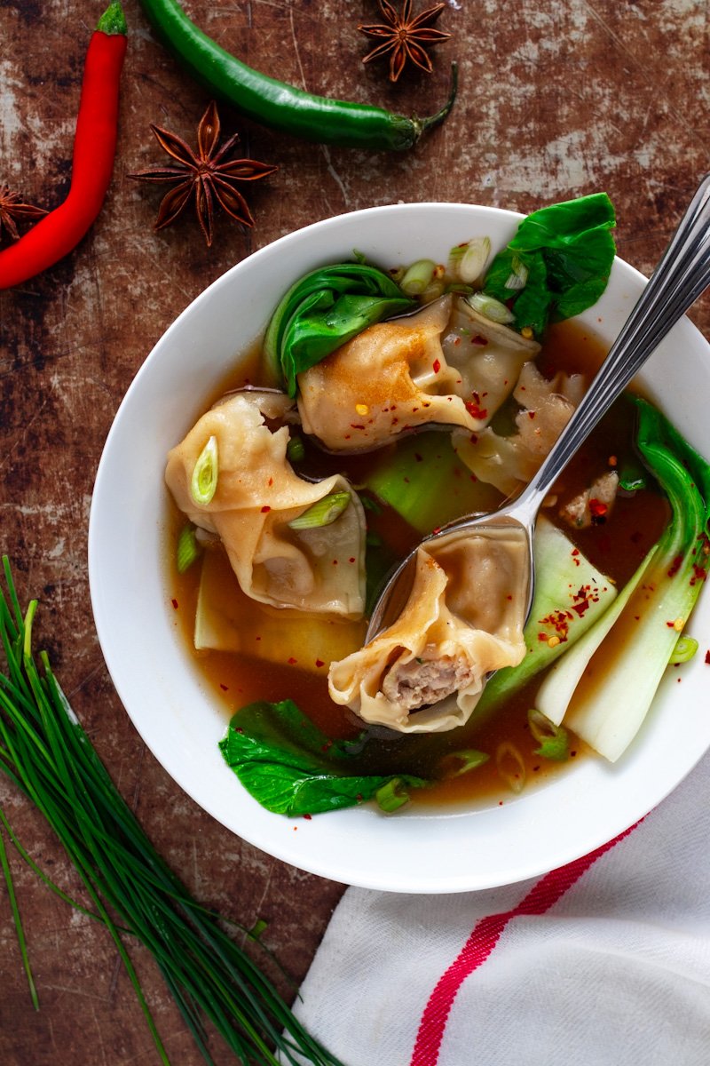 A bowl of chicken wonton soup with bok choy seen from above.