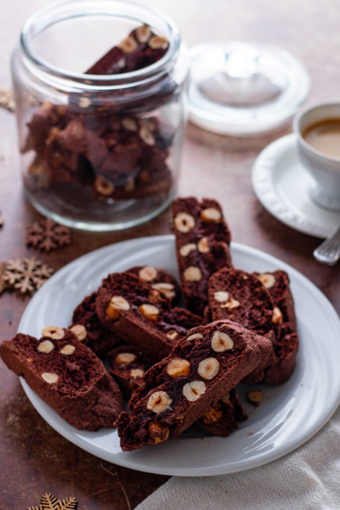 Chocolate hazelnut biscotti on a plate with a cookie jar and an espresso in the background.