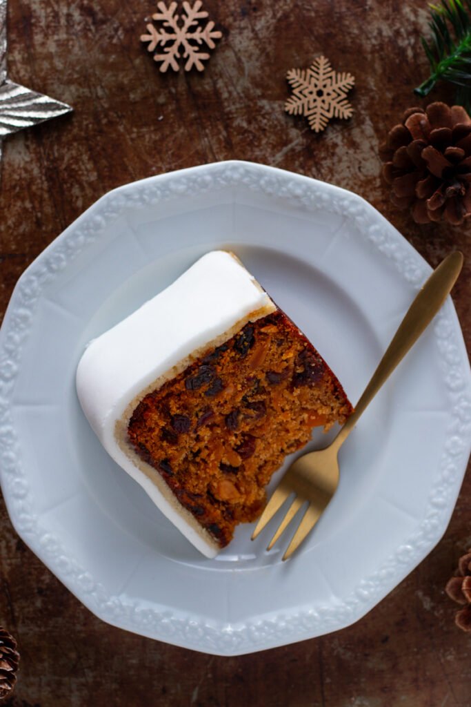 A slice of Christmas cake on a plate with a gold cake fork.