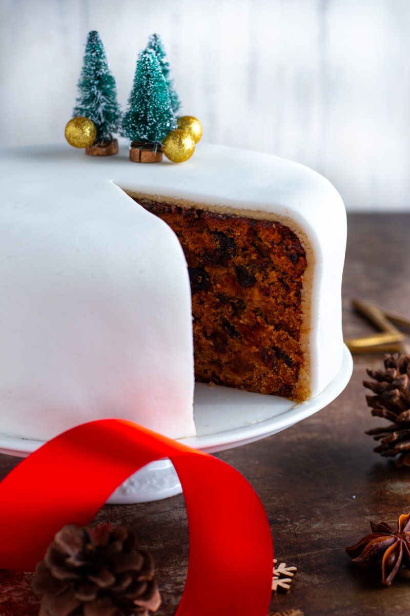 A Christmas cake on a cake stand with a slice removed showing the interior.
