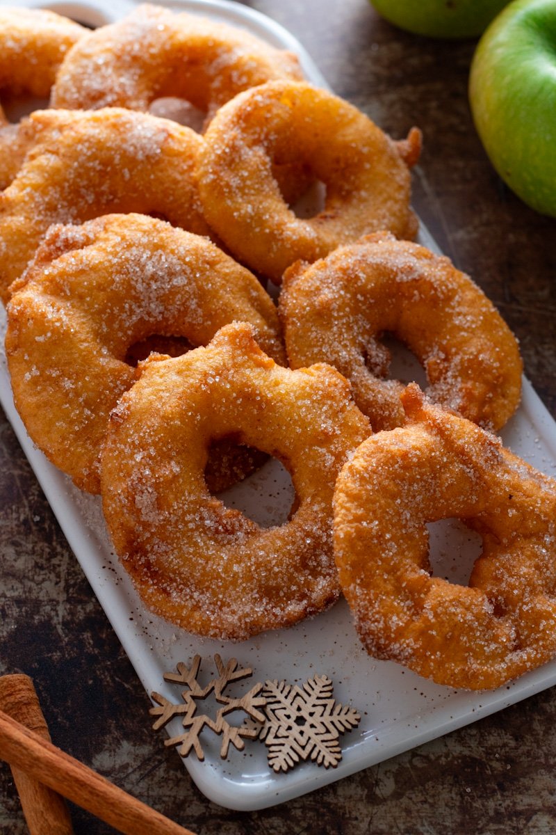 Deep Fried Apple Rings on a plate with cinnamon and apples in the background.