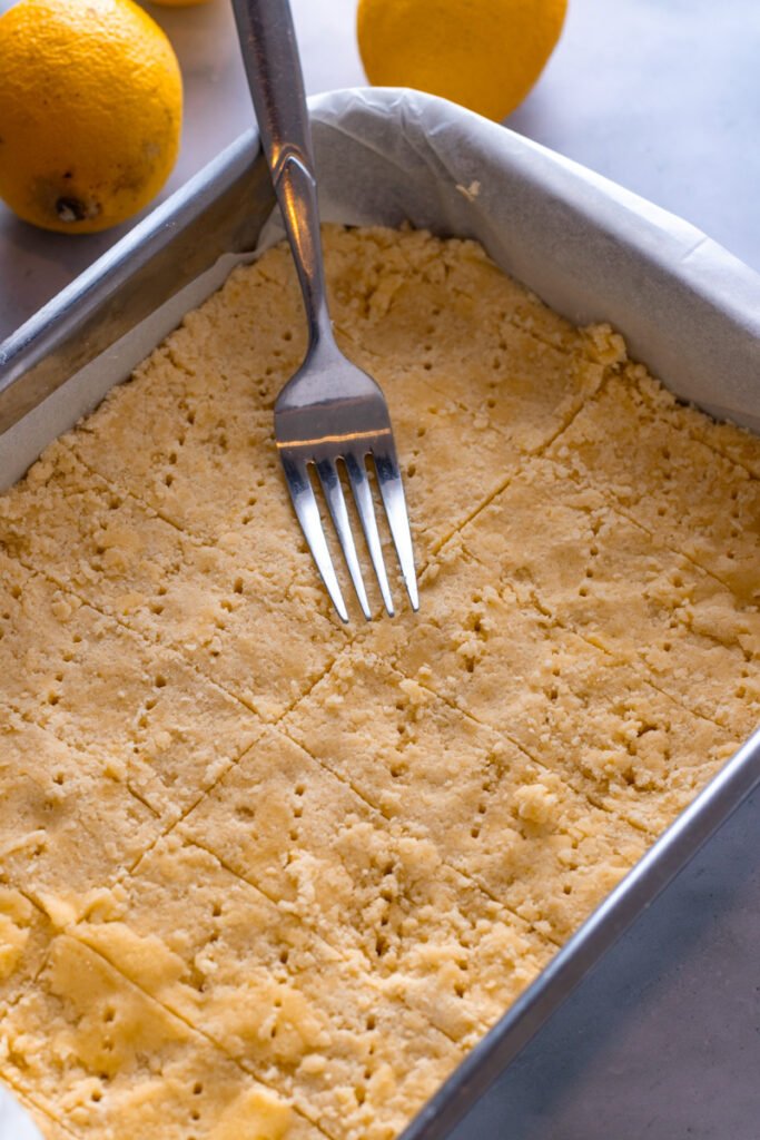 Pressed and docked lemon shortbread dough in a baking dish.