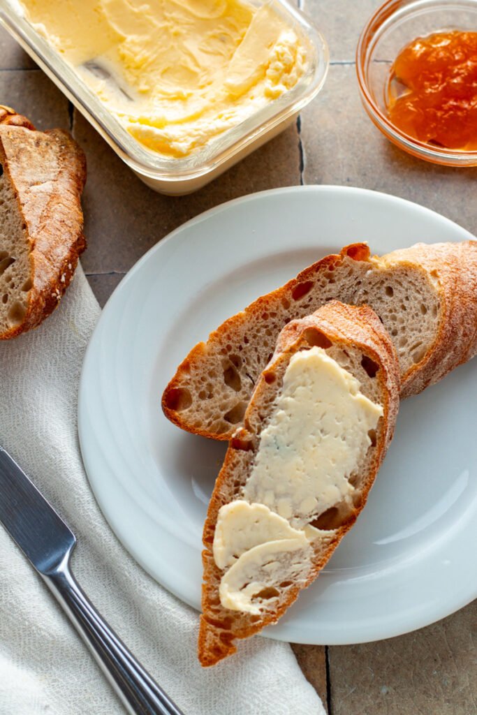 Fresh bread slices on a plate with spreadable butter and a dish of apricot jam.