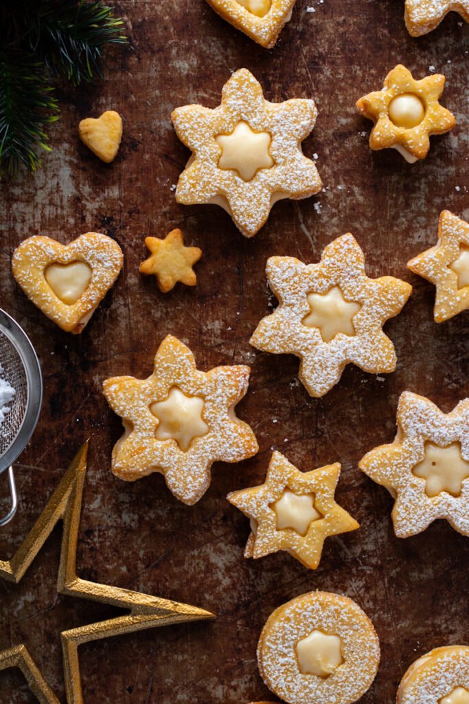 Star chaped Linzer cookies on a baking sheet filled with egg liqueur.