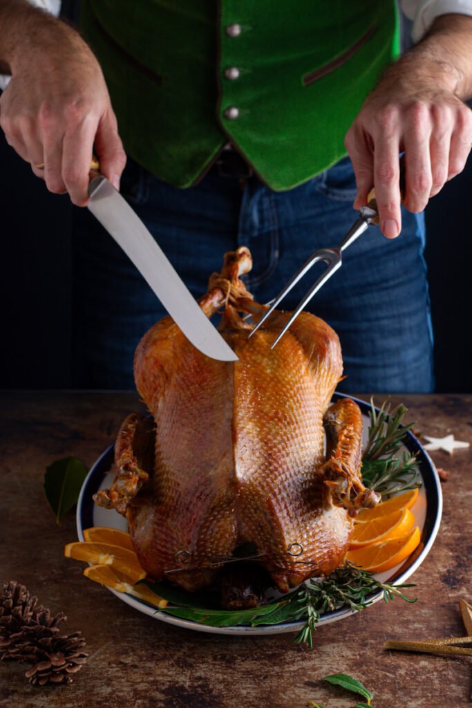 A man in a green waistcoat carving a roast goose.