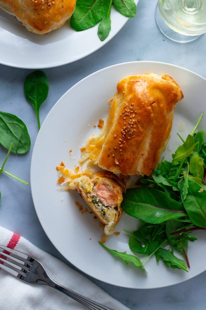 Salmon en Croûte or Sal,mon Wellington on a plate with fresh green salad and a glass of wine.