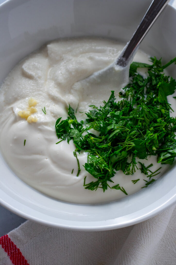 Yoghurt, salt, garlic, dill and parsley on a table.